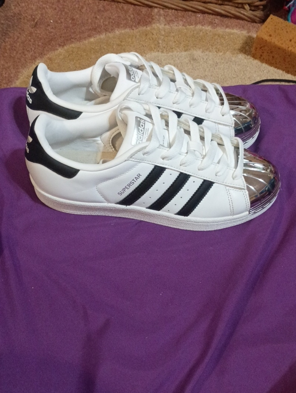 Super Stars adidas White Sneakers with Black Stripes and Metallic Silver Toe.